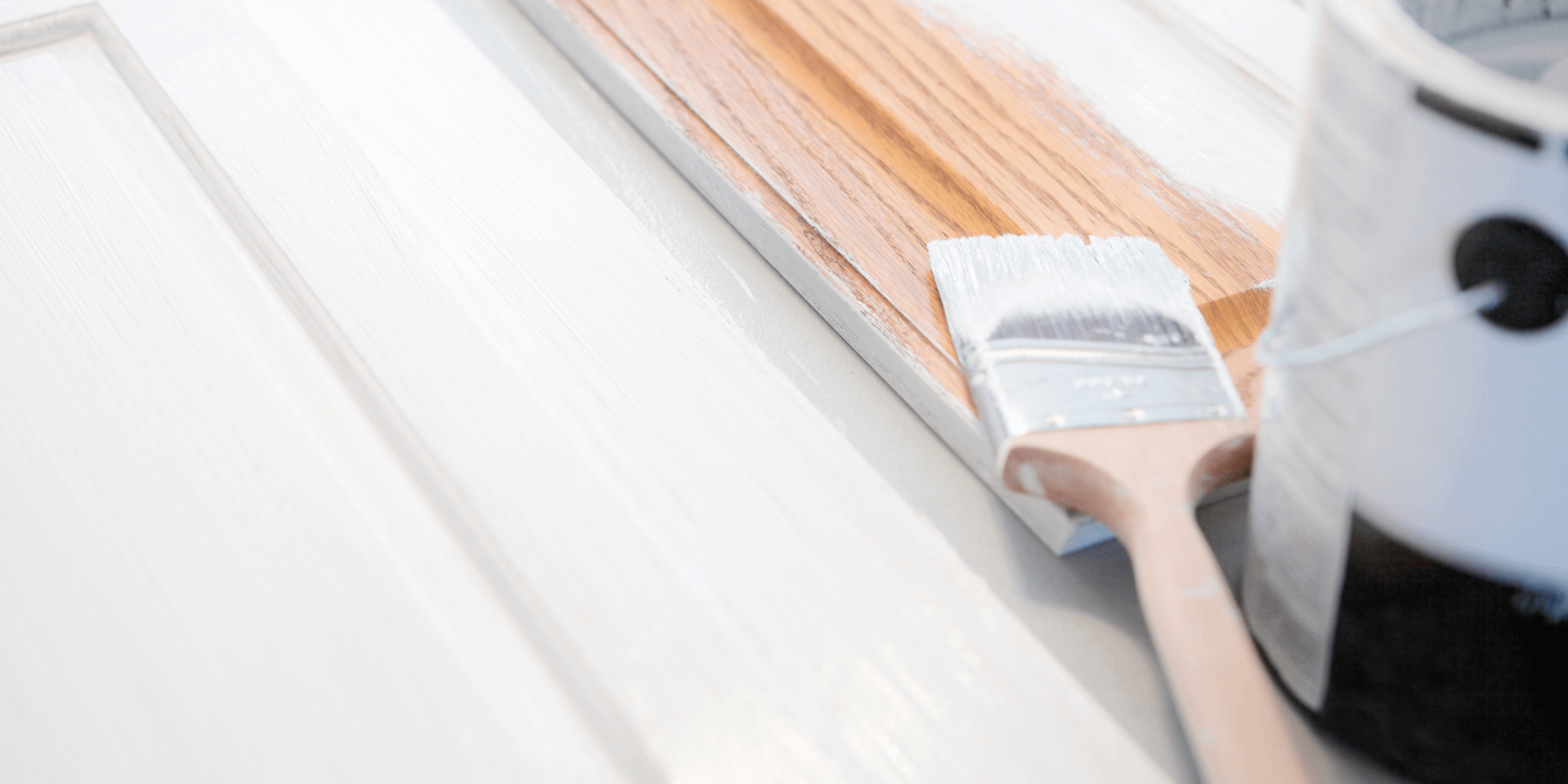 A wooden paint brush covered in white paint sits on top of wooden cabinets. On the right, a large white paint can.