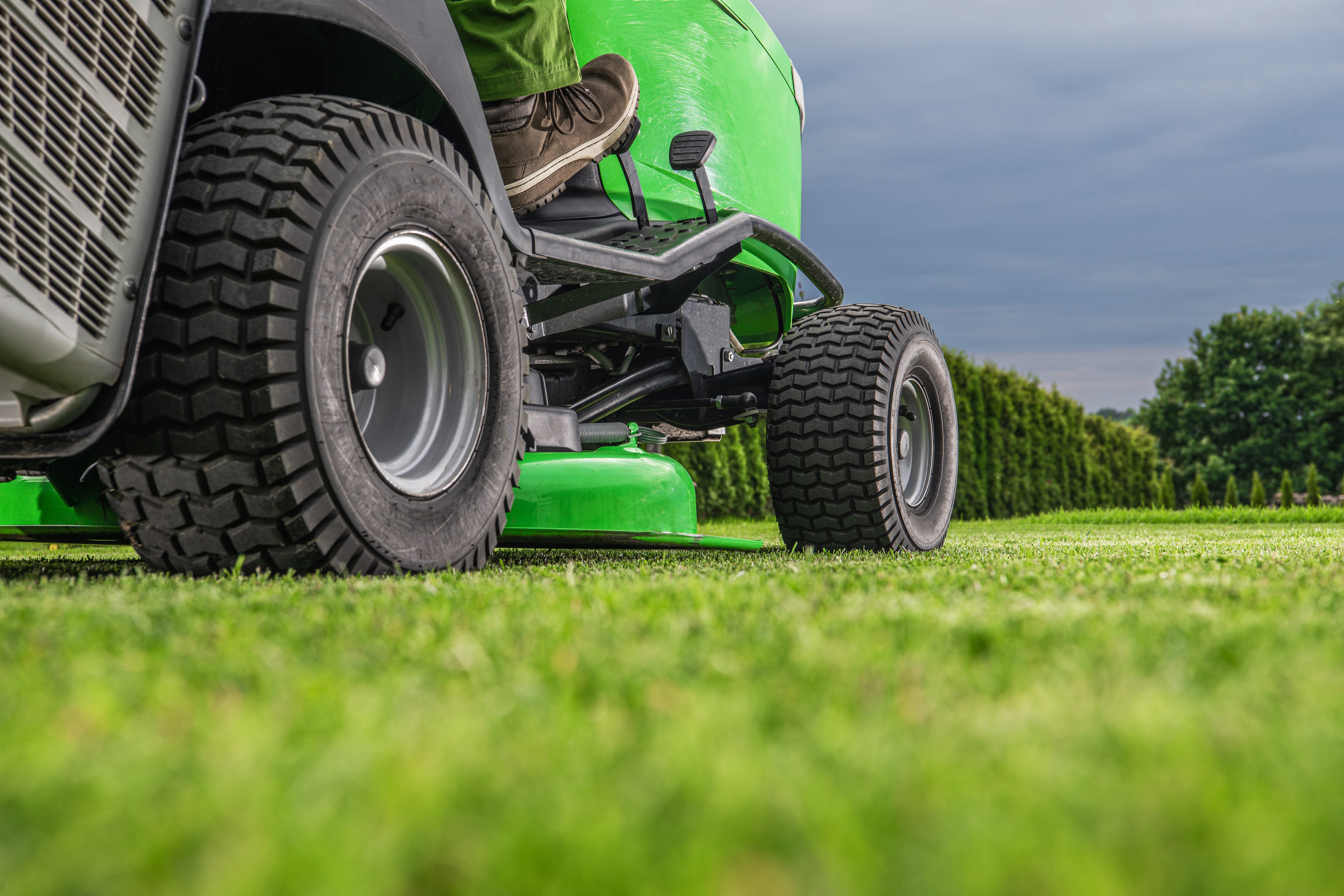 Green tractor with large wheels mowing grass on a sunny day