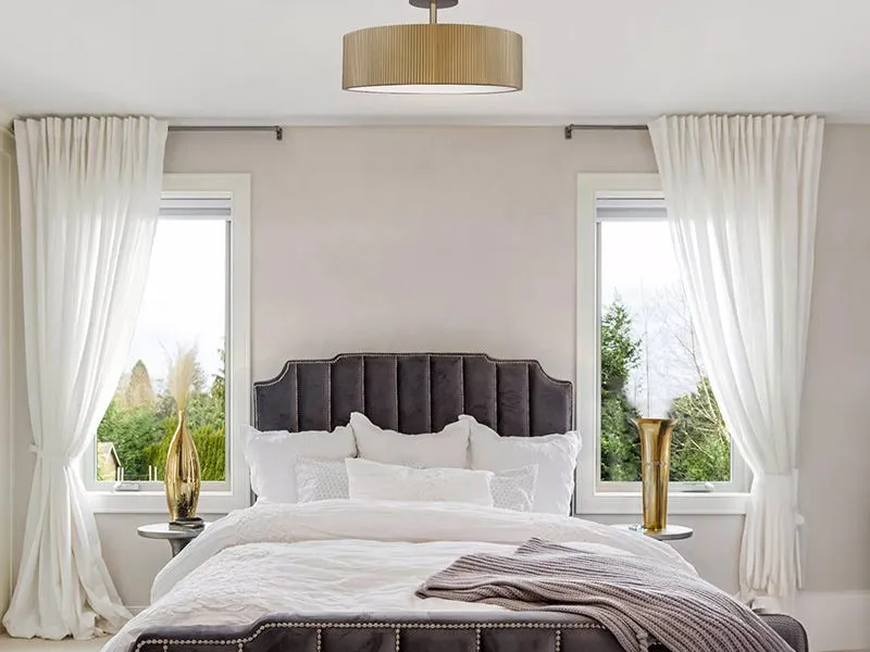 Elegant bedroom featuring a drum-shaped ceiling light between two windows
