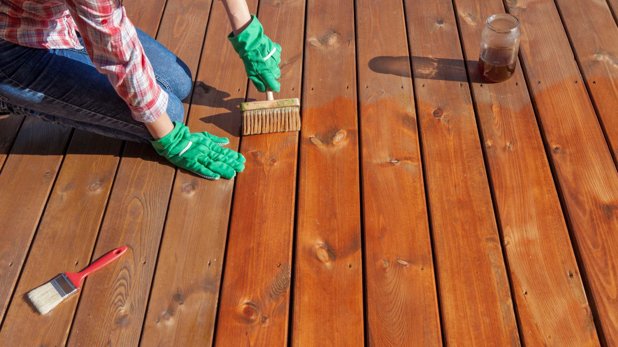 person applying transparent stain to a deck with brush