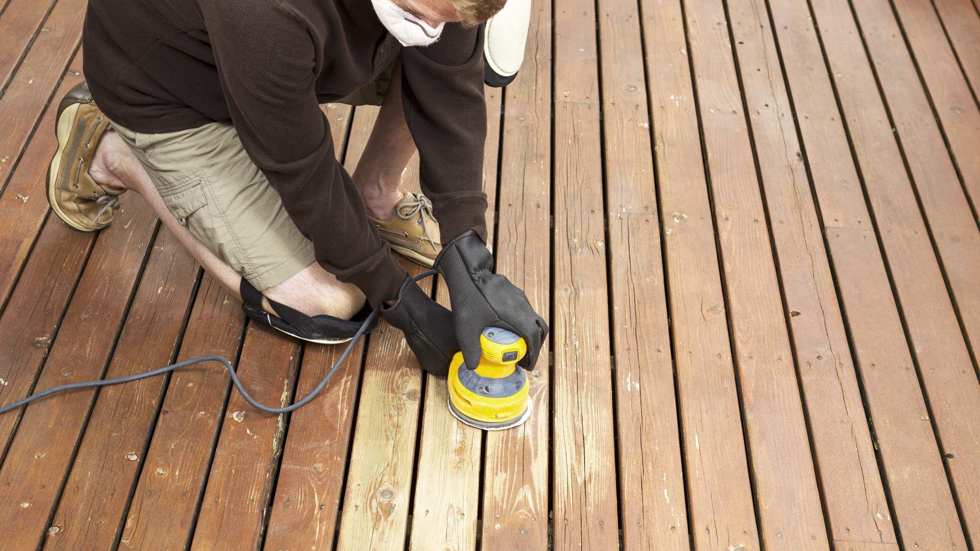 person sanding a deck with an electric sander