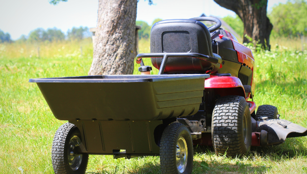 Red tractor with large wheels with barrel attachement at the back. Bright green mowed grass can be seen under the tractor.