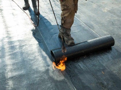 Person installing rolled roofing with torch