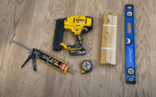 caulking in caulking gun, nailer, measuring tape, pack of shims, and level